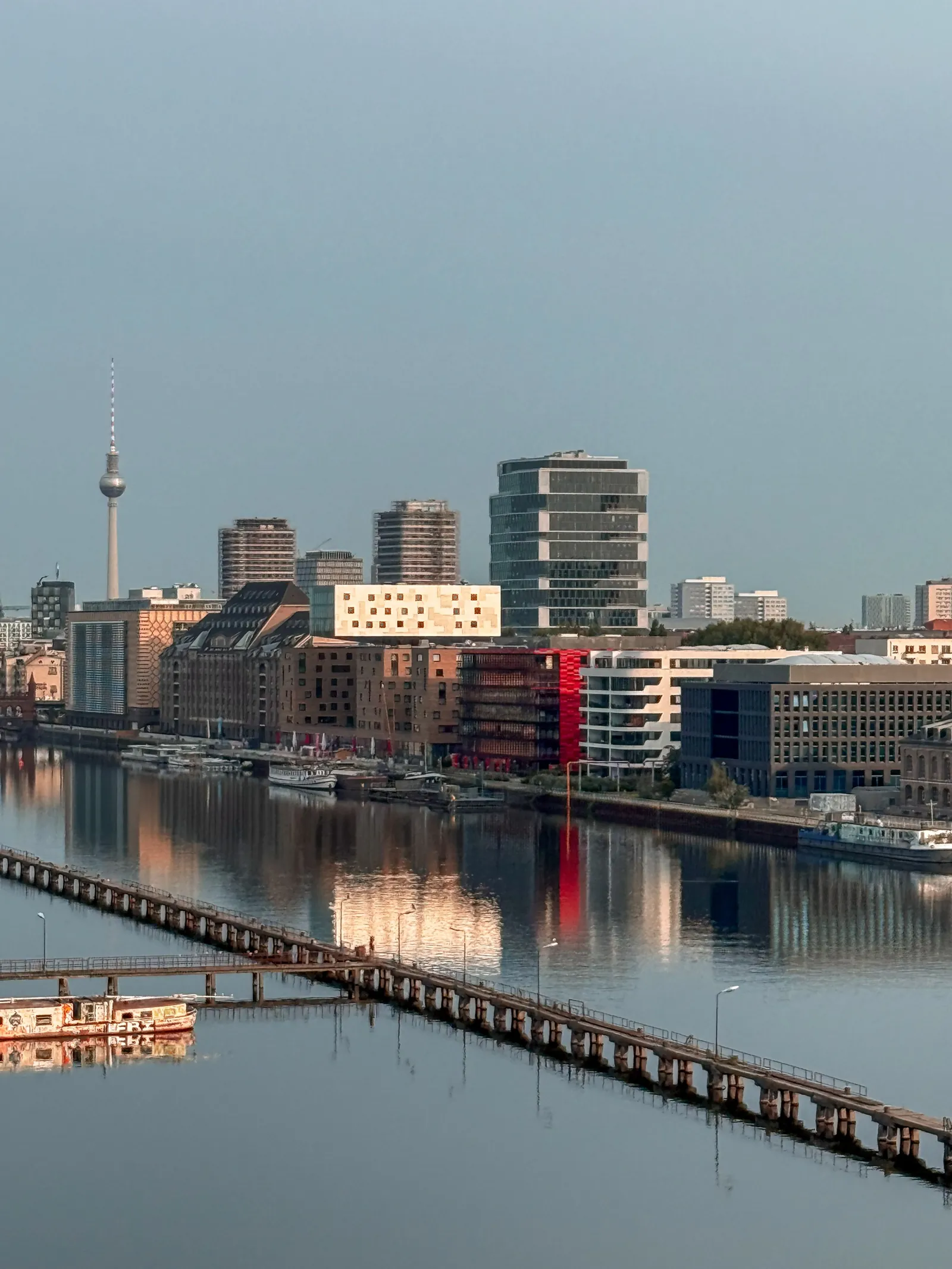 Morning on the Spree in Berlin: the TV Tower, new buildings and old warehouses reflected in still water.